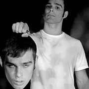 Black and white photo of a boy standing, holding his own head.